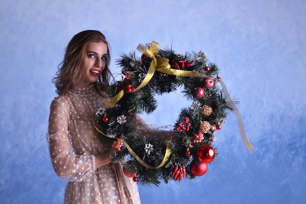 Mulher bonita com guirlanda de natal nas mãos sobre fundo azul