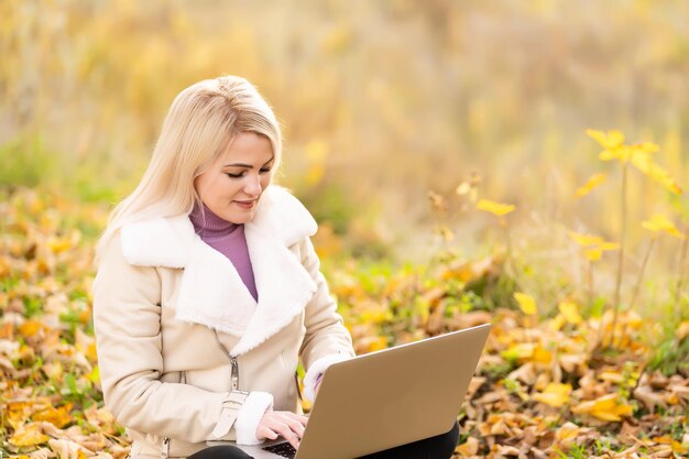Mulher bonita com laptop no parque outono. Cena da beleza da natureza com fundo de folhagem colorida, árvores amarelas e folhas no outono. Outono estilo de vida ao ar livre. Mulher feliz e sorridente nas folhas de outono