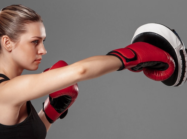 Mulher bonita com luvas vermelhas lutando boxe em fundo cinza