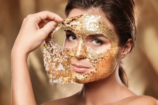 Mulher bonita com máscara dourada brilhante no rosto para tratamento de pele
