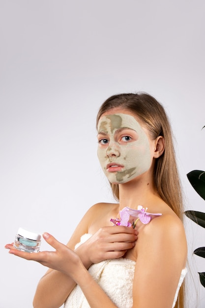 Mulher bonita com máscara facial verde ramo de orquídea e creme nas mãos