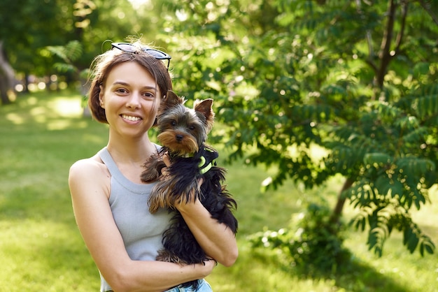 Mulher bonita com o pequeno Yorkshire Terrier em um parque ao ar livre