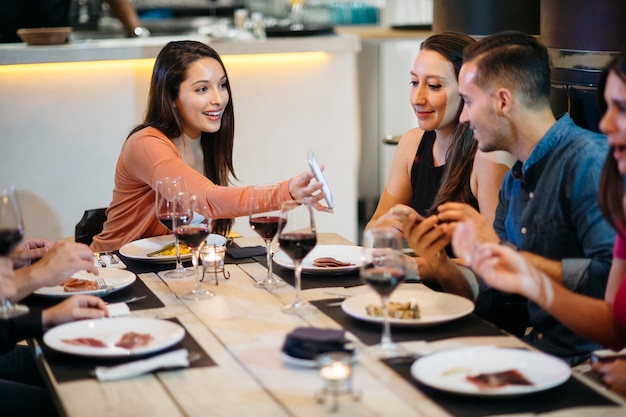 Mulher bonita com o smartphone no jantar com os amigos