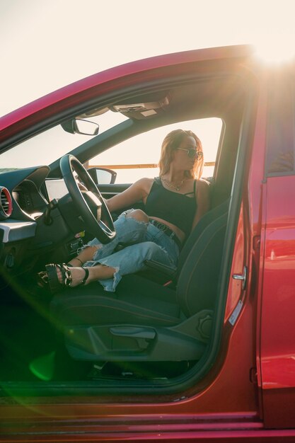 Foto mulher bonita com óculos de sol está posando dentro de um carro ao pôr do sol