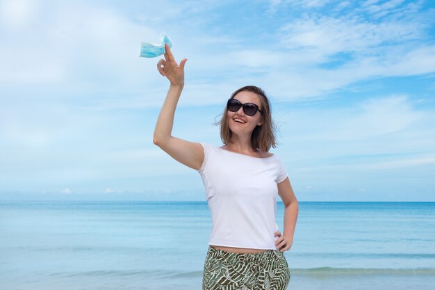 Mulher bonita com óculos de sol pretos segurando uma máscara médica