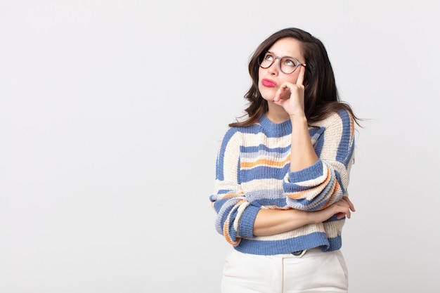 Mulher bonita com olhar concentrado, imaginando com uma expressão duvidosa, olhando para cima e para o lado