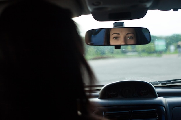 Mulher bonita com olhos bonitos está olhando no espelho retrovisor em um carro preto.