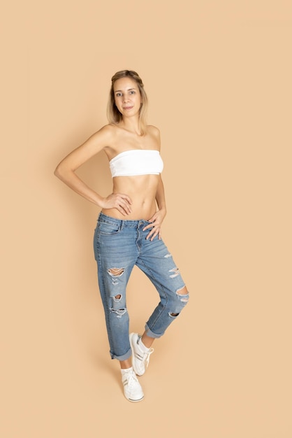 Mulher bonita com resíduos magros sorrindo e posando usando sutiã branco e jeans rasgados azuis