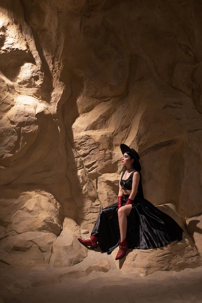 Foto mulher bonita com roupas pretas sexy, sentada na rocha na moda canyon nas montanhas