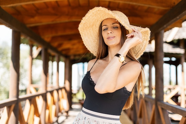 Mulher bonita com um chapéu de palha trançado na praia e uma camiseta de renda preta caminhando em um dia de folga de verão