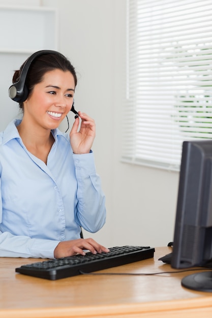 Mulher bonita com um fone de ouvido ajudando clientes enquanto está sentado