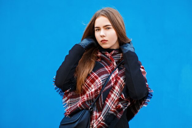 Mulher bonita com um lenço e um casaco posando perto de uma parede azul brilhante