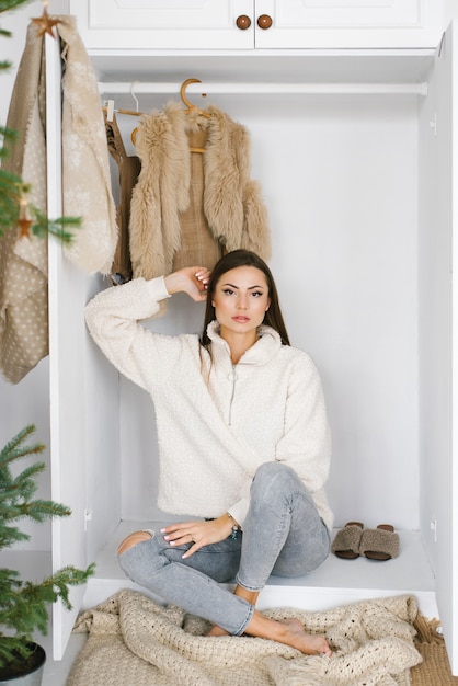 Foto mulher bonita com um suéter bege sentada no armário