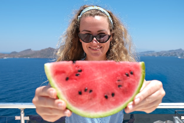 Foto mulher bonita com uma fatia de melancia fatia de melancia vermelha com vista para o mar