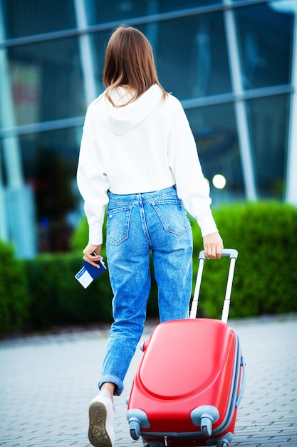Mulher bonita com uma mala perto do aeroporto, em viagem.
