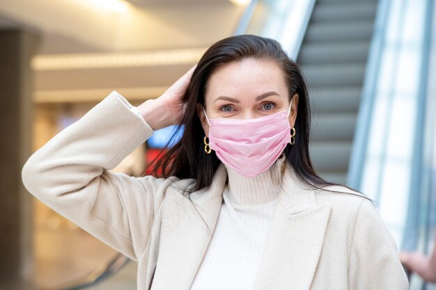 Mulher bonita com uma máscara médica rosa no rosto contra o fundo da escadadora em um