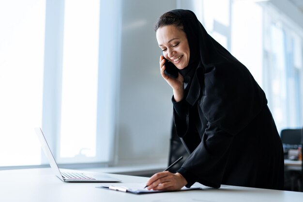 Mulher bonita com vestido abaya trabalhando em seu computador. funcionária de meia idade no trabalho em um escritório de negócios em dubai. conceito sobre culturas e estilo de vida do oriente médio