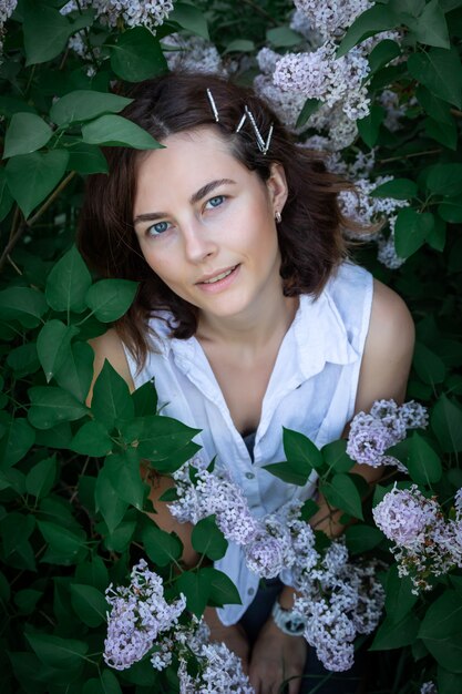 Mulher bonita com vestido floral verão posando contra o pano de fundo de uma floração de árvores lilás