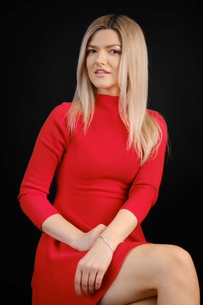 Mulher bonita com vestido vermelho sentada na cadeira no estúdio escuro