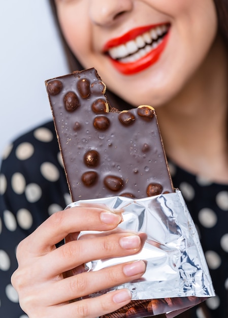 Mulher bonita come chocolate com nozes. Lábios vermelhos. Sorriso bonito. Foto recortada. Foco seletivo.