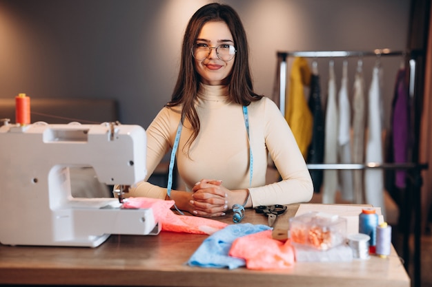 Mulher bonita costureira de óculos costurando roupas na máquina de costura