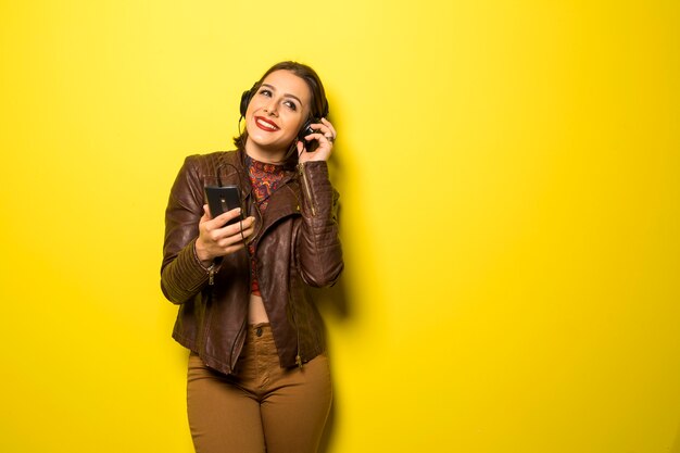 Mulher bonita curtindo música com os fones de ouvido na parede amarela