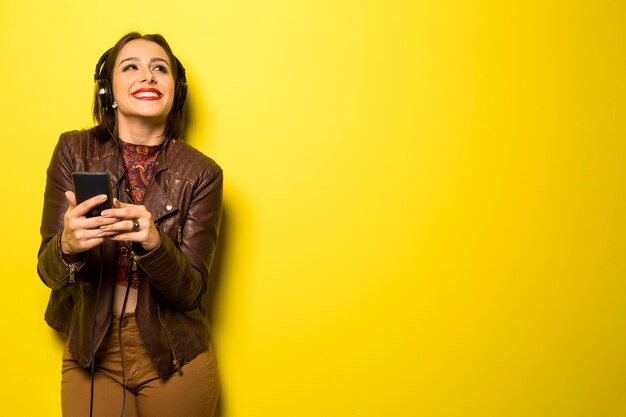 Mulher bonita curtindo música com os fones de ouvido na parede amarela