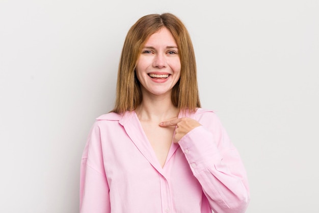 Mulher bonita de cabeça vermelha, feliz, orgulhosa e surpresa, apontando alegremente para se sentir confiante e elevada