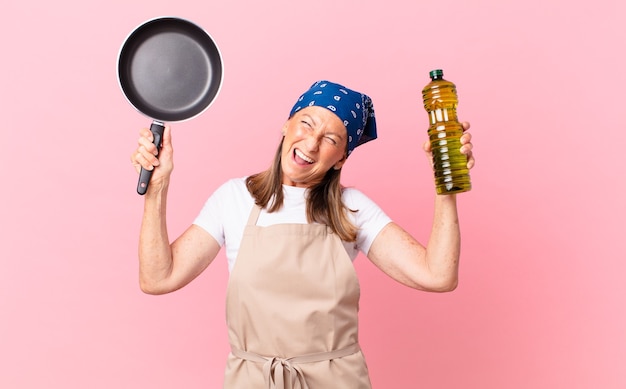 Mulher bonita de meia-idade, chef segurando uma panela e uma garrafa de azeite