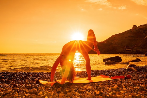Mulher bonita de meia idade com cabelo preto fazendo Pilates com o anel no tapete de ioga perto do mar na praia de seixos Conceito de ioga de fitness feminino Harmonia e meditação de estilo de vida saudável