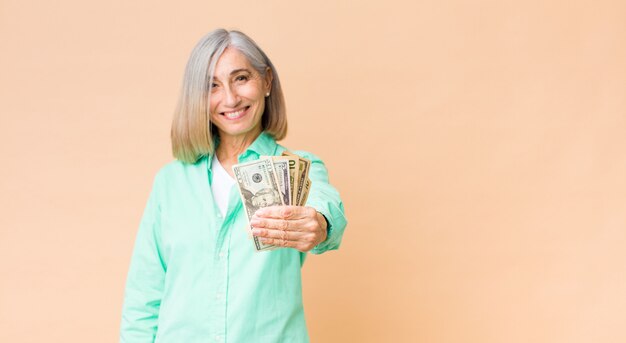 Foto mulher bonita de meia idade com notas de dólar contra a parede do espaço de cópia