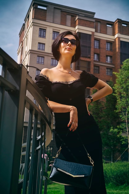 mulher bonita de meia idade em um vestido preto e chapéu passeia pelo parque da cidade e rua