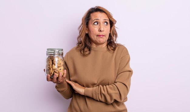 Mulher bonita de meia-idade encolhendo os ombros, sentindo-se confusa e incerta. conceito de biscoitos caseiros