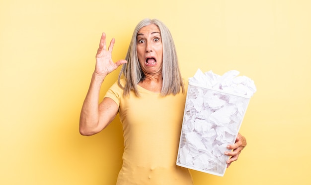 Mulher bonita de meia-idade gritando com as mãos no ar. conceito de falha de bolas de papel