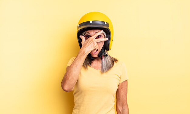 Mulher bonita de meia-idade parecendo chocada, assustada ou apavorada, cobrindo o rosto com a mão. conceito de capacete de motocicleta