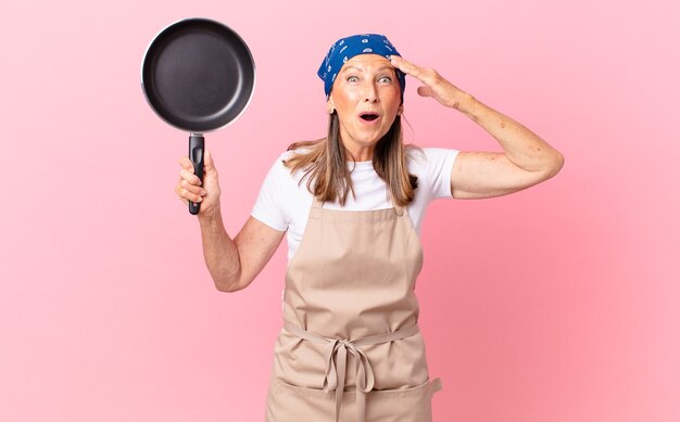 Mulher bonita de meia-idade parecendo feliz, espantada e surpresa e segurando uma panela. conceito de chef