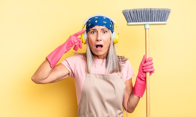 Foto mulher bonita de meia-idade parecendo surpresa, percebendo um novo pensamento, ideia ou conceito. conceito de casa e vassoura