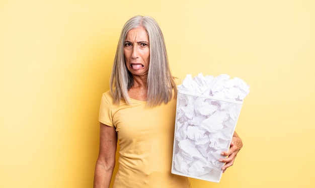 Mulher bonita de meia-idade se sentindo enojada e irritada e com a língua de fora. conceito de falha de bolas de papel