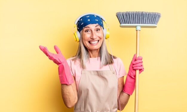 Mulher bonita de meia-idade se sentindo feliz, surpresa ao perceber uma solução ou ideia. conceito de casa e vassoura