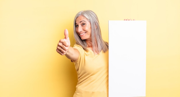 Mulher bonita de meia-idade se sentindo orgulhosa, sorrindo positivamente com o polegar para cima. conceito de tela vazia