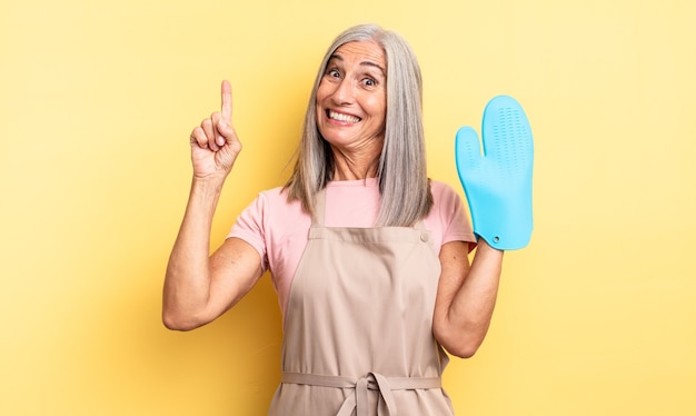 Mulher bonita de meia-idade se sentindo um gênio feliz e animado depois de realizar uma ideia. conceito de luva de forno