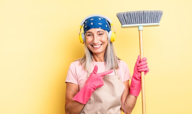 mulher bonita de meia-idade sorrindo alegremente, sentindo-se feliz e apontando para o lado. conceito de casa e vassoura