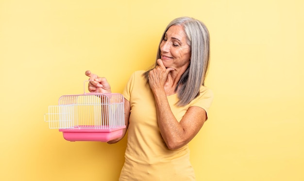 Mulher bonita de meia-idade, sorrindo com uma expressão feliz e confiante com a mão no queixo. conceito de gaiola ou prisão para animais de estimação