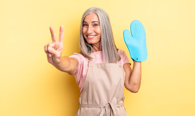 Mulher bonita de meia-idade sorrindo e parecendo amigável, mostrando o número dois. conceito de luva de forno