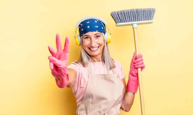 Mulher bonita de meia-idade, sorrindo e parecendo amigável, mostrando o número três. conceito de casa e vassoura