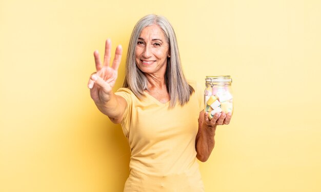 Mulher bonita de meia-idade, sorrindo e parecendo amigável, mostrando o número três. conceito de garrafa de doces