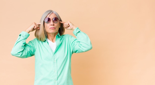 Mulher bonita de meia-idade, usando óculos escuros contra a parede