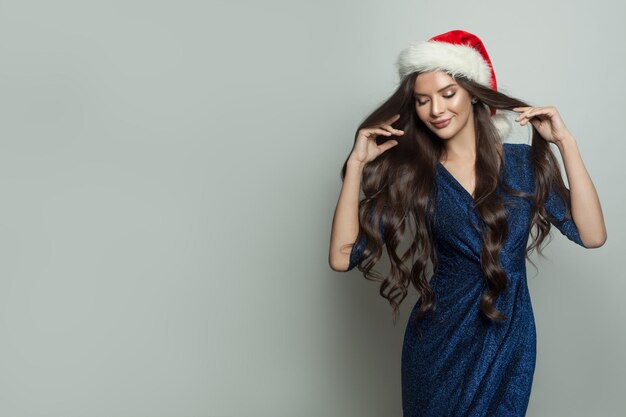 Mulher bonita de moda com chapéu de Papai Noel posando no feriado branco de Natal e festa de Ano Novo