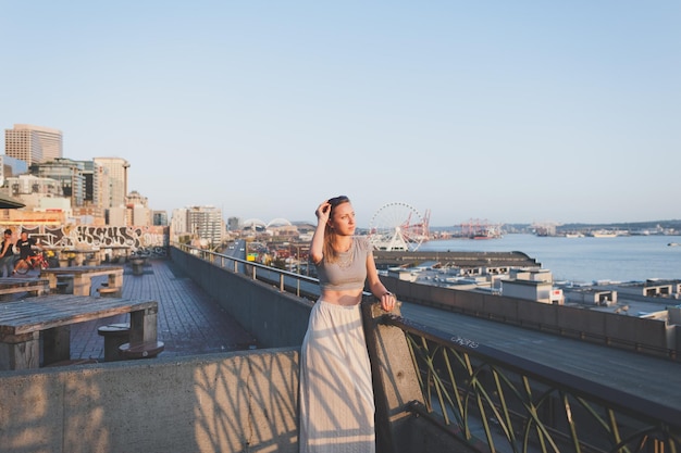 Foto mulher bonita de pé no terraço da construção na cidade contra o céu claro