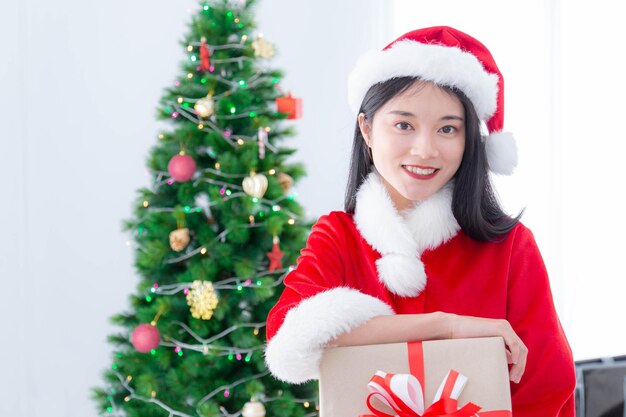 Mulher bonita de vestido de Papai Noel com caixa de presentes e fundo de árvore de Natal